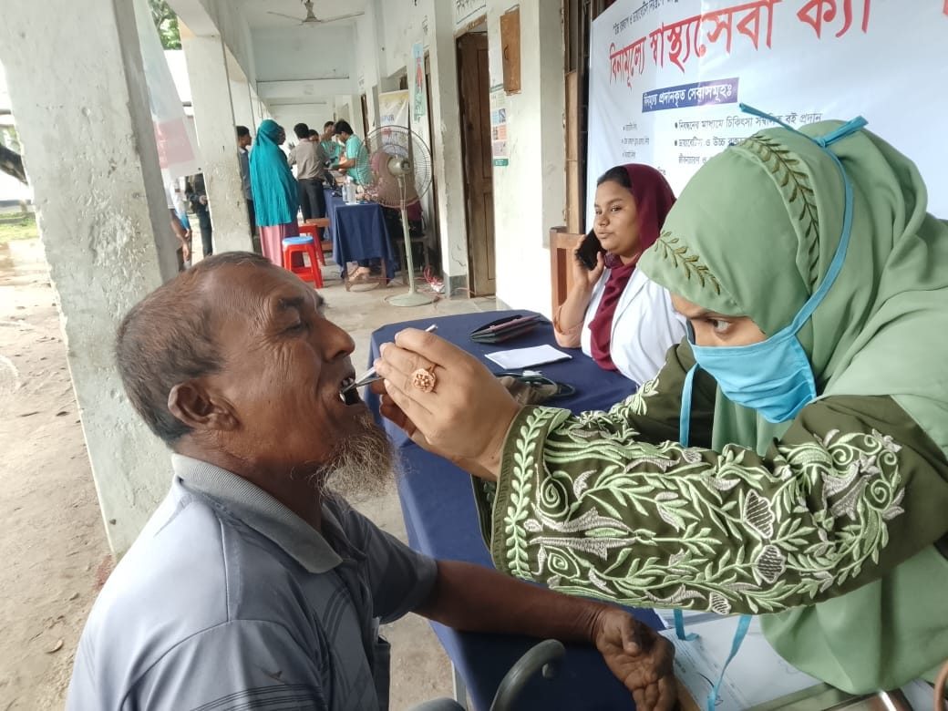 A medical professional examining an elderly man's mouth at the camp, with a Free Healthcare Camp banner in the background